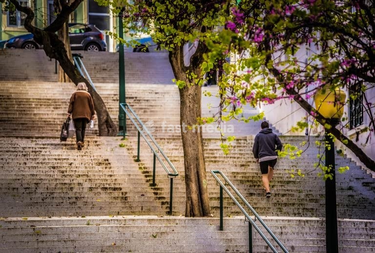 People climbing historic stone steps with blooming bougainvillea trees in Lisbon's hilly neighborhoods, Portugal