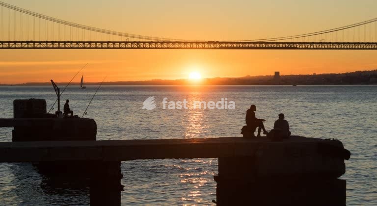 Fishermen silhouetted at sunset before the 25 de Abril Bridge, Tagus River, Lisbon, Portugal