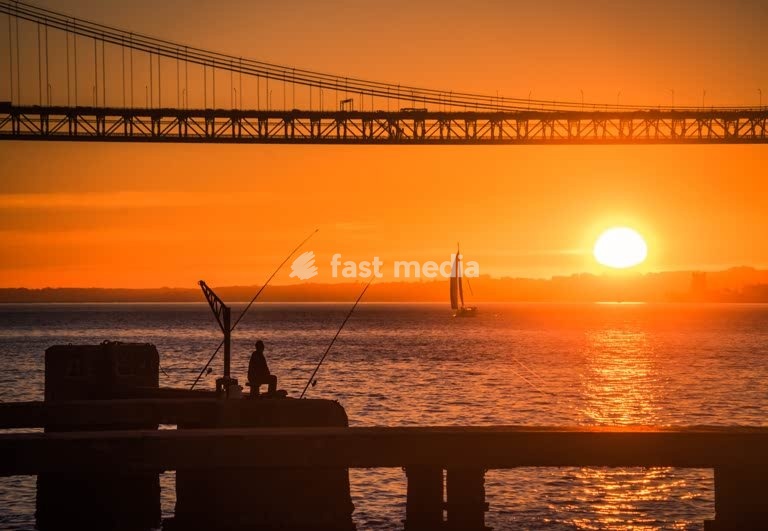 Fisherman silhouette under the 25 de Abril Bridge at sunset, Tagus River, Lisbon, Portugal