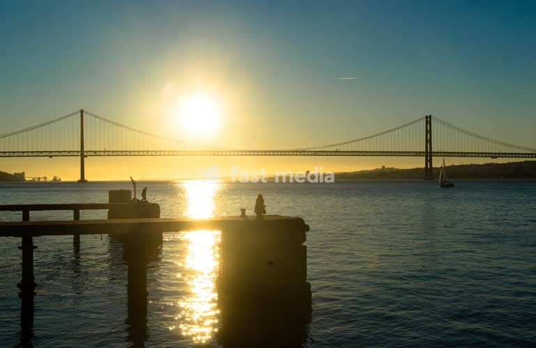 Fishermen silhouetted at sunset before the 25 de Abril Bridge, Tagus River, Lisbon, Portugal