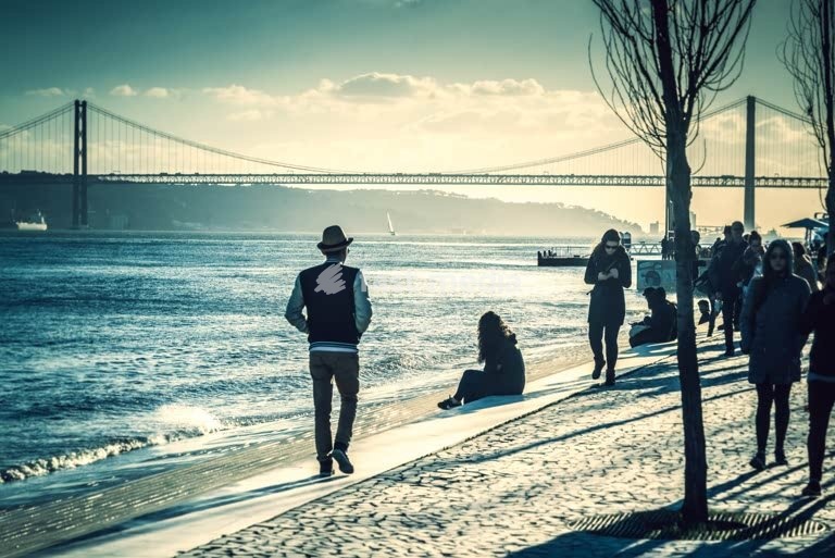 People relaxing on the riverside beach at Ribeira das Naus with 25 de Abril Bridge, Lisbon