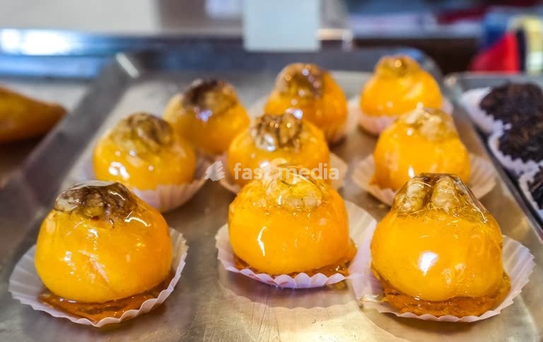 Portuguese egg-yolk pastries topped with walnuts, glossy caramel glaze, traditional Lisbon bakery treat