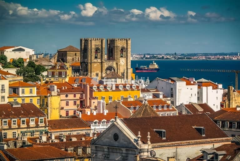 Lisbon Cathedral towers rising above the rooftops of Baixa, Tagus River beyond, Portugal