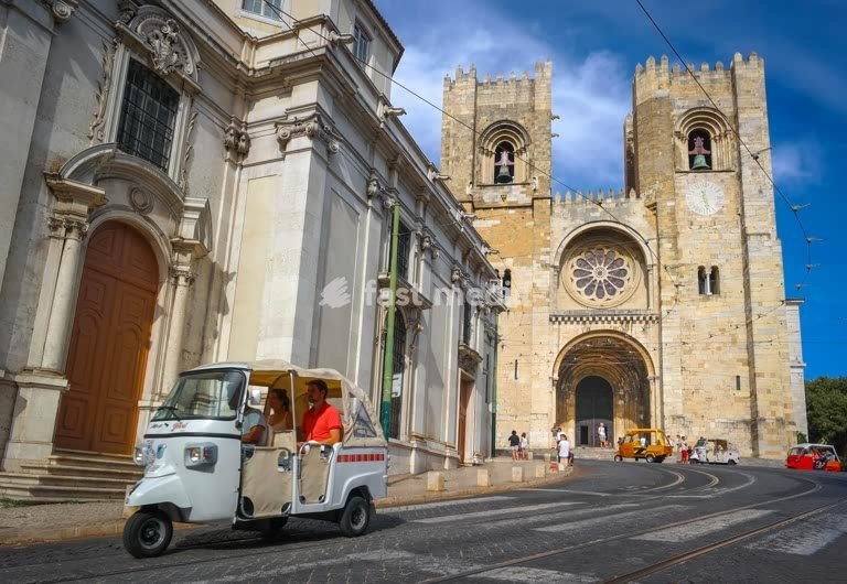 Lisbon. Tourists avoiding the steep climb by taking a Tuk-tuk. Cathedral Zé in the background.