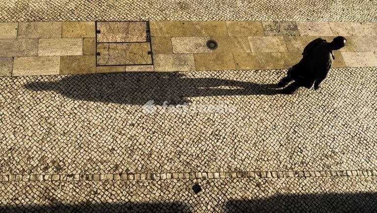 Lisbon, Portugal. Man with a long shadow walking down Rua Barros Queirós near Rossio square in the afternoon light. Typical limestone pavement