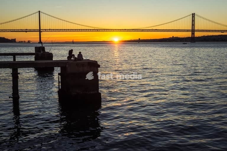 Fishermen silhouetted at sunset, 25 de Abril Bridge, Lisbon, tranquil riverside evening scene