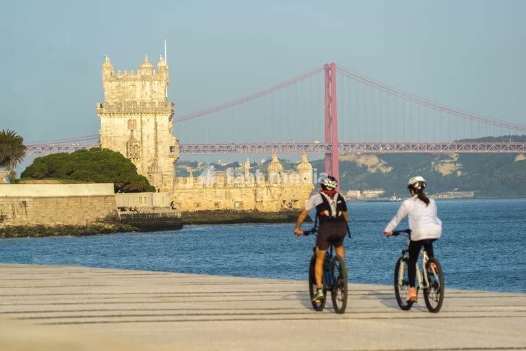 Cyclists riding Tagus riverside path, Belém Tower and 25 de Abril Bridge, Lisbon waterfront lifestyle