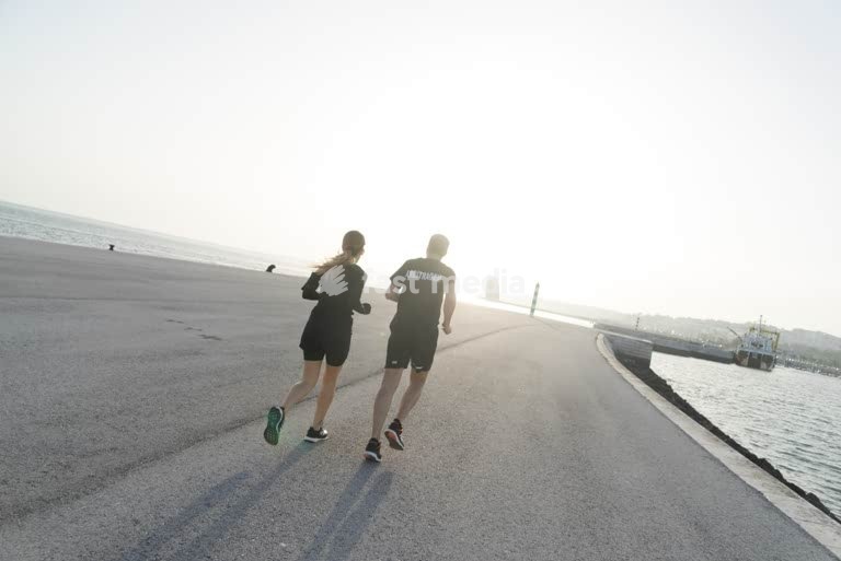 Couple jogging along the waterfront in Lisbon at sunrise, enjoying a peaceful morning workout by the Tagus River with soft light and clear skies