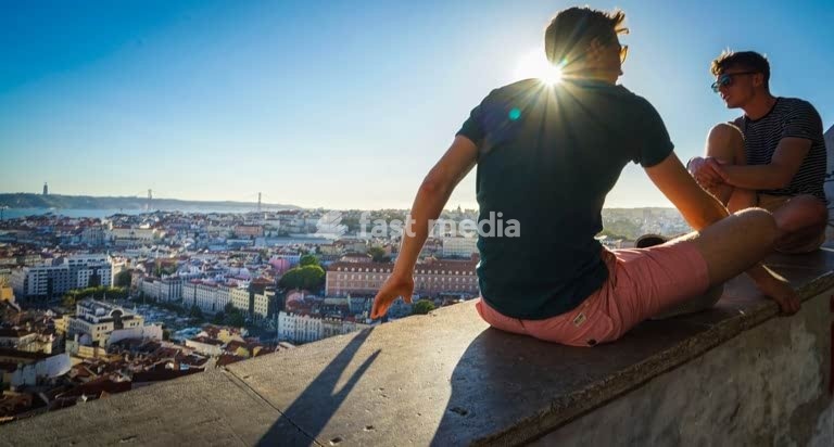 Two men enjoying sunset city view from Miradouro da Graça, Lisbon, Portugal, backlit sun flare