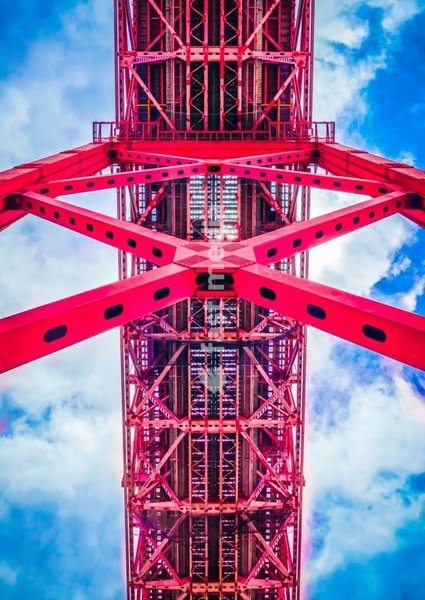 Red steel truss structural details of 25 de Abril suspension bridge in Lisbon, Portugal. Engineering architecture against blue sky