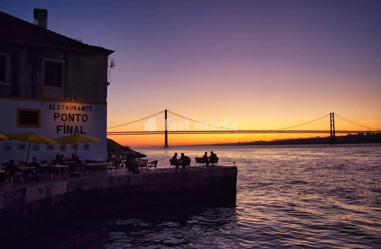 Lisbon, Portugal. Restaurant Ponto Final in Almada.Silhouettes of people watching sunset over Tagus River with 25 de Abril Bridge in background
