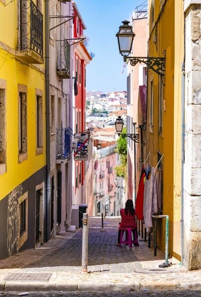 Narrow cobblestone street with traditional colorful buildings and historic street lamps in Lisbon's old town, Portugal