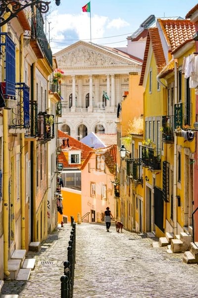 Narrow cobblestone street with traditional buildings and historic street lamps in Lisbon's São Bento district, with the parliament in the background