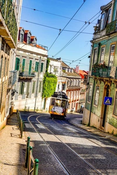 Historic yellow tram 25E navigates narrow cobblestone street in Lisbon's charming Lapa district surrounded by traditional Portuguese architecture