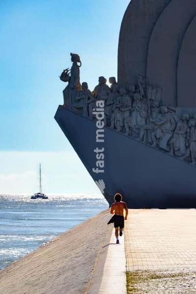 A healthy young man running along the Tagus river towards the Monument of the Discoveries in Lisbon, Portugal