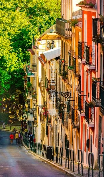 Colorful facades and wrought iron balconies in a steep street of Lisbon’s Bairro Alto district. Sunny afternoon in Portugal’s capital.