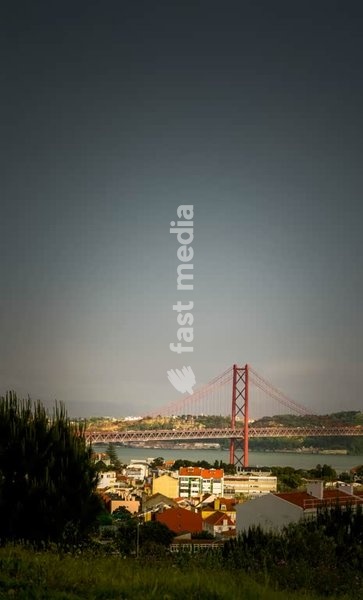 View of Lisbon’s iconic 25th April Bridge spanning the Tagus River, with rooftops and soft evening light adding depth and serenity to the scene