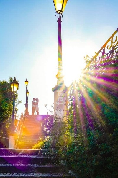 Secret Lisbon: A romantic couple stands on sunlit stairs in Lapa, Lisbon surrounded by vintage lamps and lush greenery