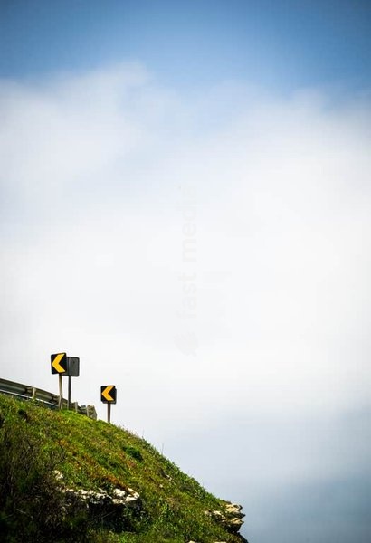 Yellow warning road signs indicating sharp curve ahead on grassy hillside symbolizing importance of careful driving and road safety