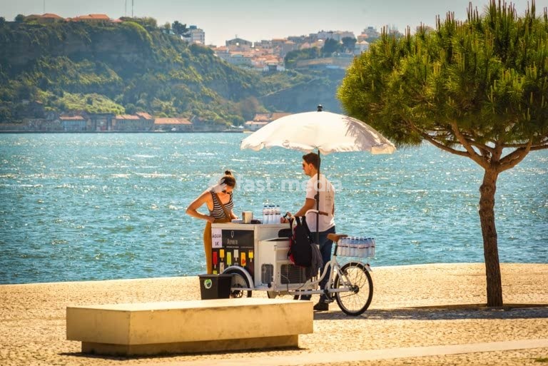 Street vendor with mobile cart and umbrella sells refreshments along the Tagus River waterfront promenade in Lisbon, Portugal, Europe