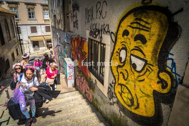 Young women walking up steps in Bairro Alto district of Lisbon, Portugal. Funny graffiti comment on overtourism. Photo Peter Delius