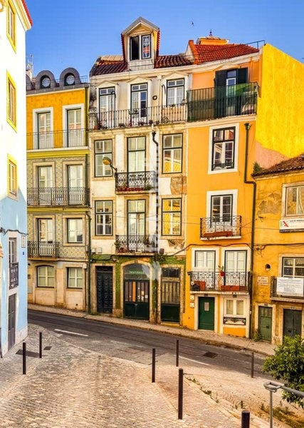 Colorful traditional Portuguese buildings with wrought iron balconies line a narrow cobblestone street in historic Lisbon, Portugal, Europe