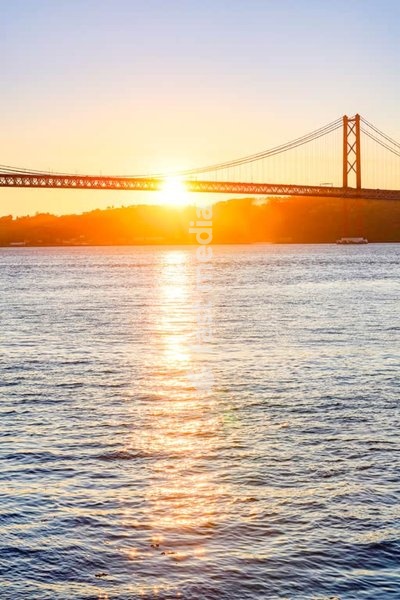 Golden sunrise behind the 25 de Abril Bridge in Lisbon, Portugal, casting a warm glow over the Tagus River in a moment of peace and beauty