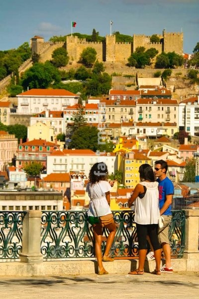 Tourists enjoy panoramic views of Castelo de São Jorge from São Pedro de Alcântara viewpoint's ornate balustrade, Lisbon, Portugal