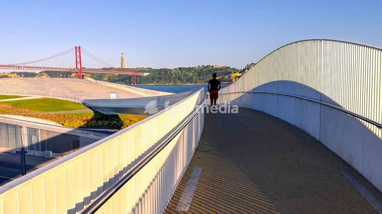 Modern curved pedestrian walkway at MAAT Museum in Belém, Lisbon, with iconic 25 de Abril Bridge visible in background, Portugal
