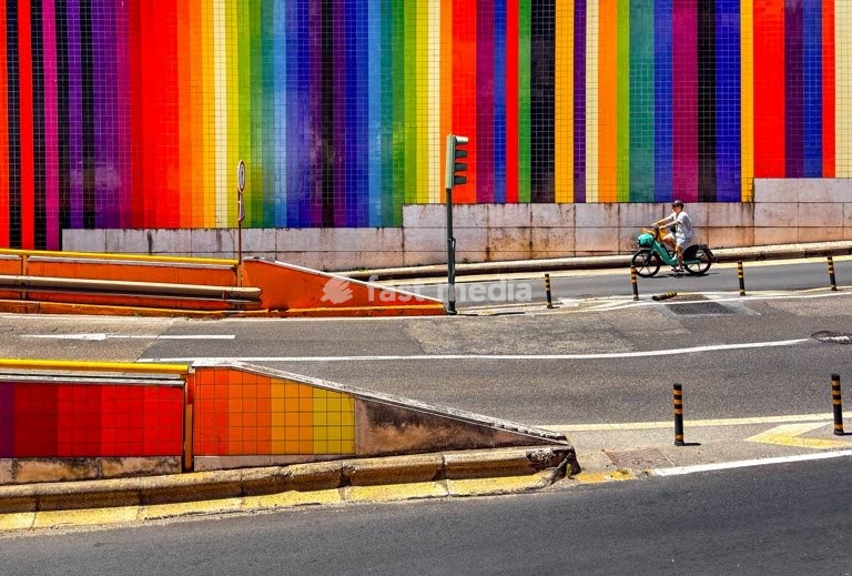 Cyclist passes a colorful tiled wall on Avenida Infante Santo in Lisbon, Portugal – vibrant public art and urban scene with road infrastructure