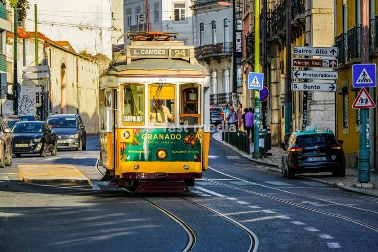 Tram 24 in Príncipe Real, Lisbon, passing through narrow city streets. The famous yellow trams are iconic symbols of the Portuguese capital