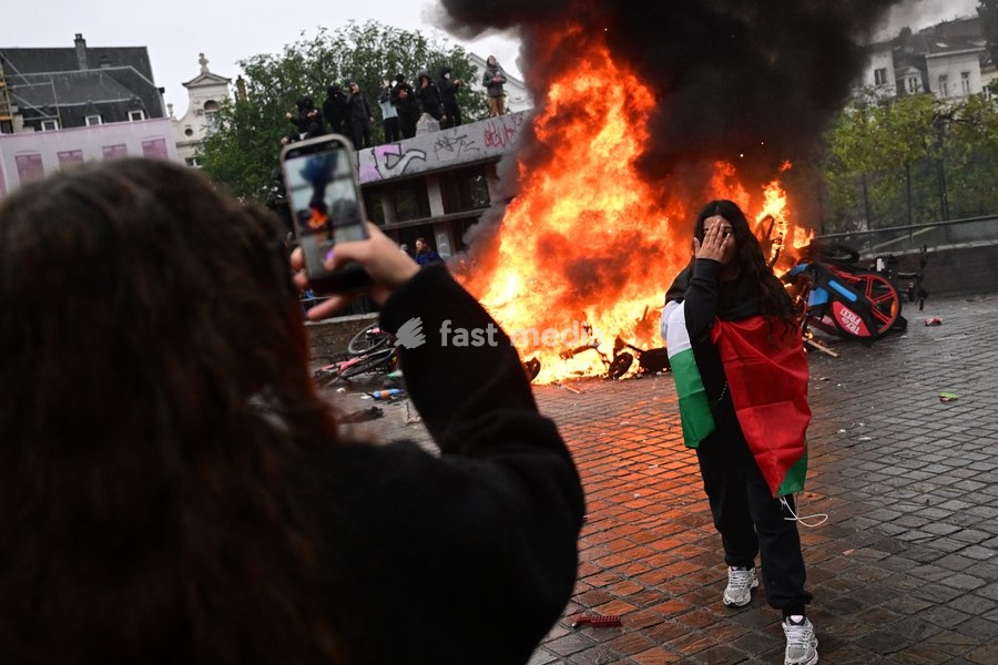 A girl poses for a picture in front of a fire of burning shared bikes during a national manifestation against the Federal Government's budgetary measures, under the 'Keep your hands out of our pockets!' (Blijf uit onze zakken! - Pas dans nos poches) moniker, organised by the trade unions on Friday…