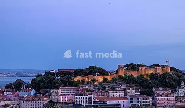 Panoramic sunset view of the Lisbon city skyline showing illuminated Saint George Castle overlooking the Tagus River