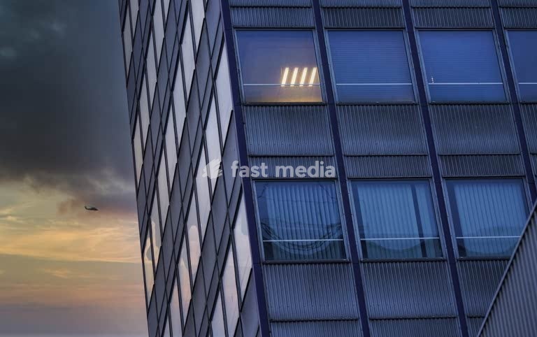 Office windows at dusk, anonymous corporate façade, solitude, isolation and urban alienation in contemporary city life. Only one room lighted