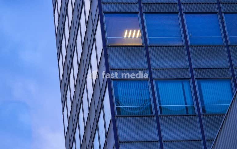 Office windows at dusk, anonymous corporate façade, solitude, isolation and urban alienation in contemporary city life. Only one room lighted
