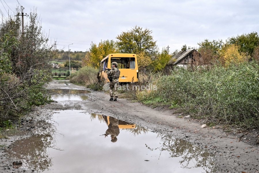 An armed Zaporizhzhian police officer walks past a puddle in the street towards a bus during a humanitarian evacuation mission for a family, including an elderly woman with limited mobility, from the settlement of Komyshuvakha, Zaporizhzhia region, Ukraine, October 19, 2026
