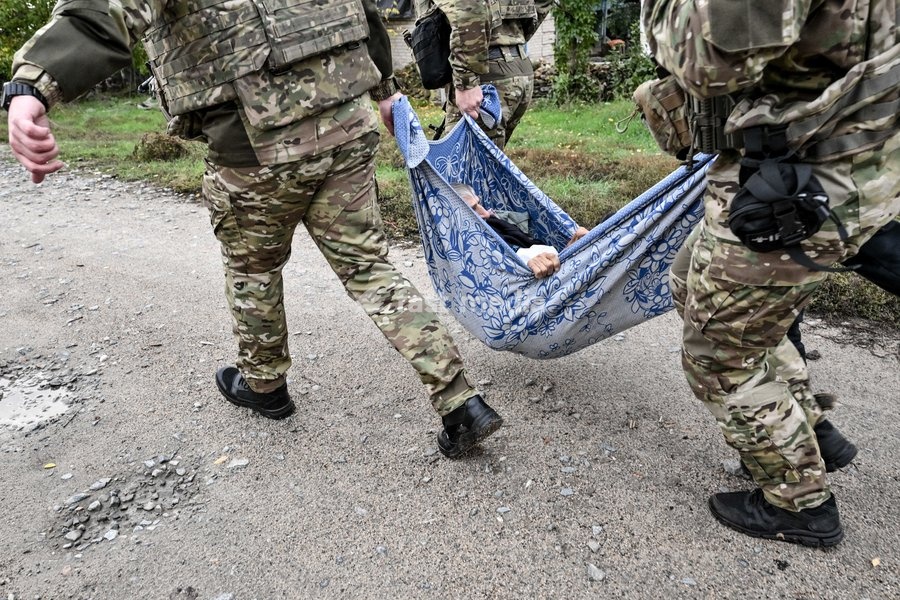 Zaporizhzhia police officers and a family member carry an elderly bedridden woman in a blanket towards a car during an evacuation from the front-line settlement of Komyshuvakha, Zaporizhzhia region, Ukraine, October 19, 2026