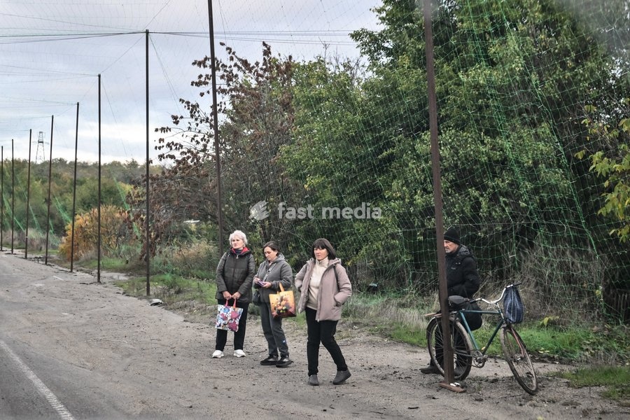 People wait for a bus by the side of the road covered with an anti-drone net in the front-line settlement of Komyshuvakha, Zaporizhzhia region, Ukraine, October 19, 2026