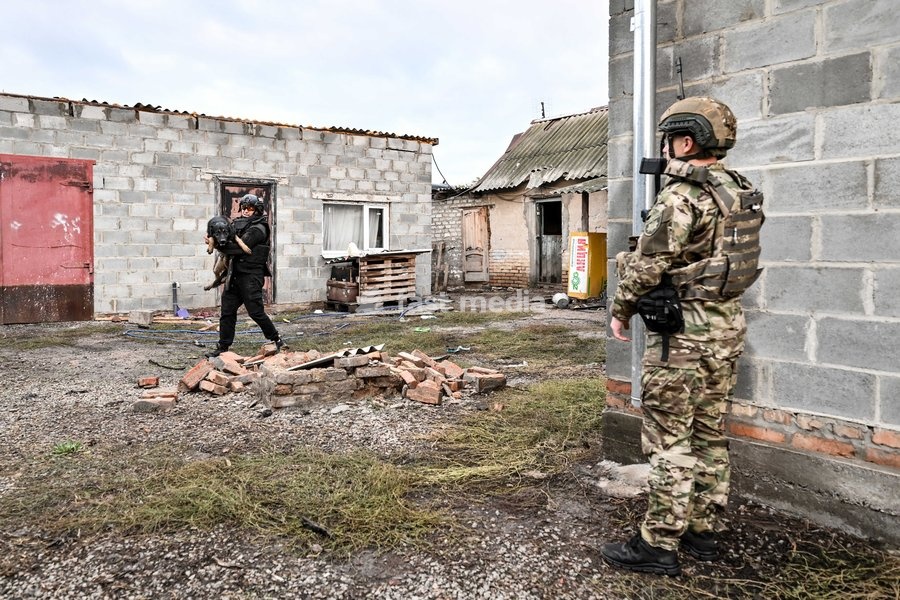 An armed Zaporizhzhia police officer stands guard as a volunteer carries a rescued dog to a minibus during a humanitarian evacuation mission in the front-line settlement of Komyshuvakha, Zaporizhzhia region, Ukraine, October 19, 2026