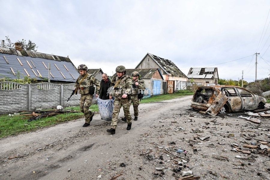 Zaporizhzhia police officers and a family member carry an elderly bedridden woman in a blanket towards a car during an evacuation from the front-line settlement of Komyshuvakha, Zaporizhzhia region, Ukraine, October 19, 2026