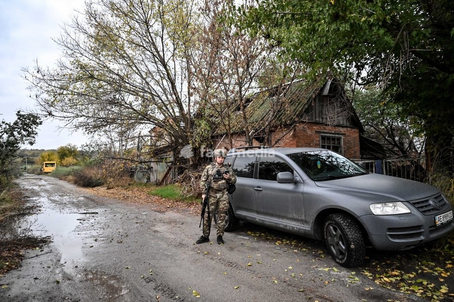 An armed Zaporizhzhian police officer stands by a car during a humanitarian evacuation mission for a family, including an elderly woman with limited mobility, from the settlement of Komyshuvakha, Zaporizhzhia region, Ukraine, October 19, 2026