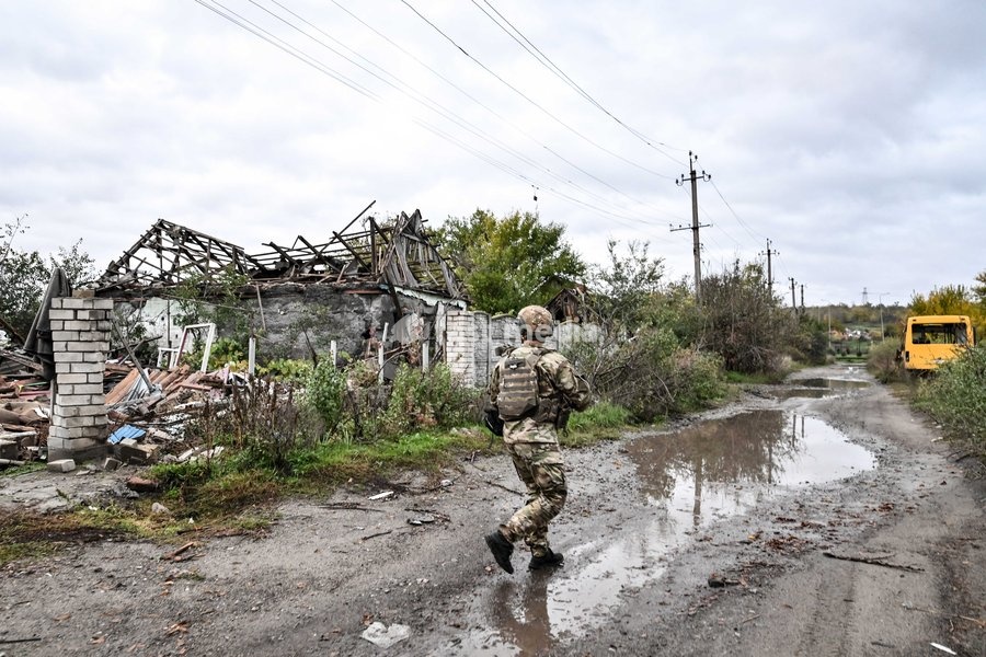An armed Zaporizhzhian police officer walks past a puddle in the street towards a bus during a humanitarian evacuation mission for a family, including an elderly woman with limited mobility, from the settlement of Komyshuvakha, Zaporizhzhia region, Ukraine, October 19, 2026
