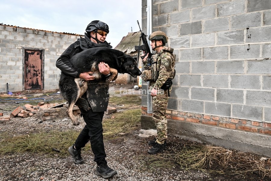 An armed Zaporizhzhia police officer stands guard as a volunteer carries a rescued dog to a minibus during a humanitarian evacuation mission in the front-line settlement of Komyshuvakha, Zaporizhzhia region, Ukraine, October 19, 2026