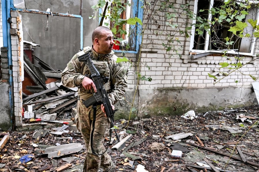 An armed Zaporizhzhia police officer walks past a house damaged by Russian bombardments during a humanitarian evacuation mission for a family with an elderly woman with limited mobility from the front-line settlement of Komyshuvakha, Zaporizhzhia region, Ukraine, October 19, 2026