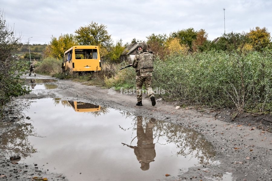 An armed Zaporizhzhian police officer walks past a puddle in the street towards a bus during a humanitarian evacuation mission for a family, including an elderly woman with limited mobility, from the settlement of Komyshuvakha, Zaporizhzhia region, Ukraine, October 19, 2026