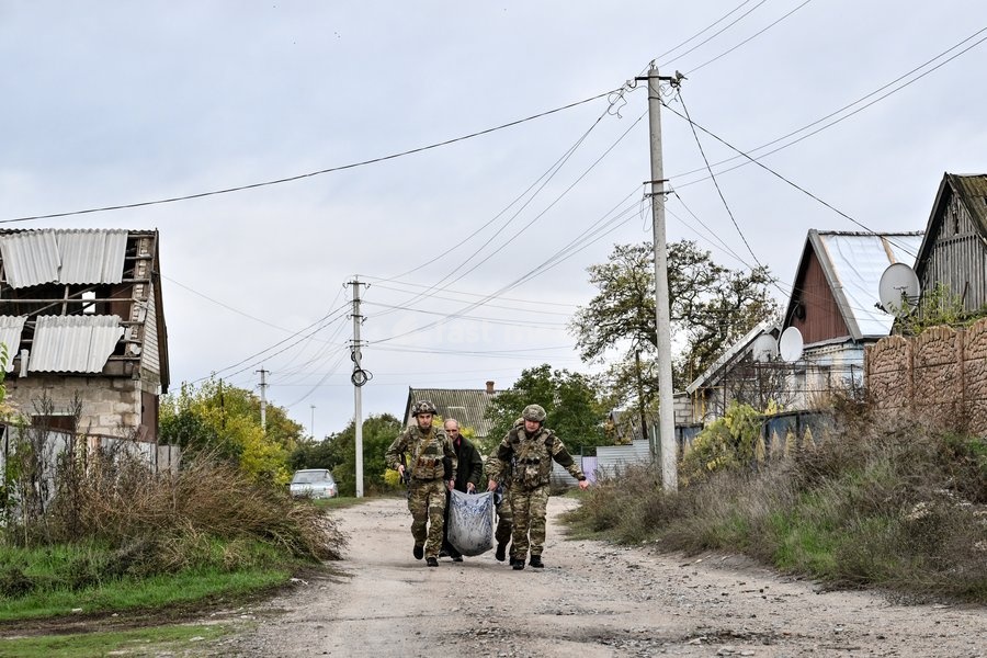 Zaporizhzhia police officers and a family member carry an elderly bedridden woman in a blanket towards a car during an evacuation from the front-line settlement of Komyshuvakha, Zaporizhzhia region, Ukraine, October 19, 2026