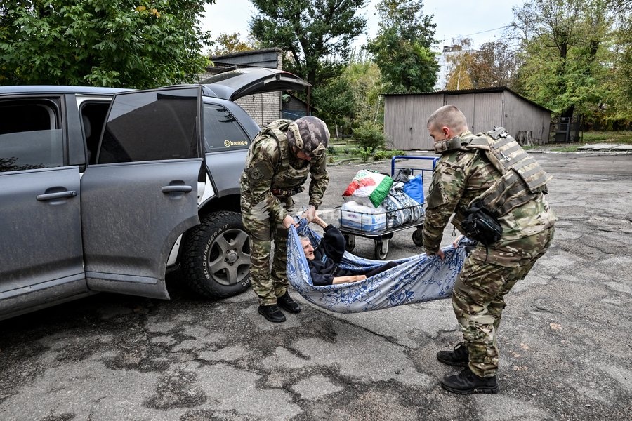 Zaporizhzhian police officers carry an elderly woman with limited mobility on a blanket from a car to a transit centre, following the evacuation of her family from the settlement of Komyshuvakha, Zaporizhzhia, Ukraine, October 19, 2026