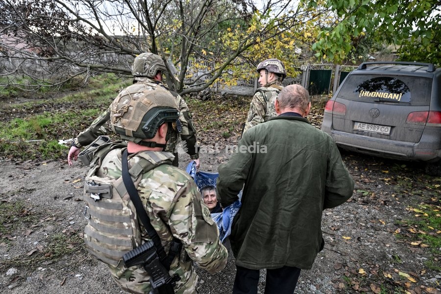 Zaporizhzhia police officers and a family member carry an elderly bedridden woman in a blanket towards a car during an evacuation from the front-line settlement of Komyshuvakha, Zaporizhzhia region, Ukraine, October 19, 2026