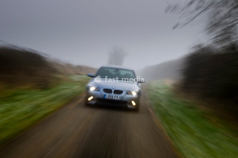 BMW 5-series car drives along empty country road in adverse foggy weather, Oxfordshire, England, United Kingdom