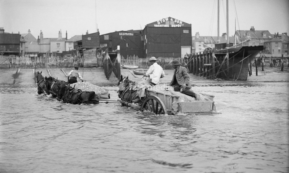 Shoreham harbour, Shoreham-by-Sea, West Sussex, 1905-1925. A partly submerged horse-drawn ballast cart in the sea off Shoreham Harbour, in front of the premises of Stow and Son Yacht Builders